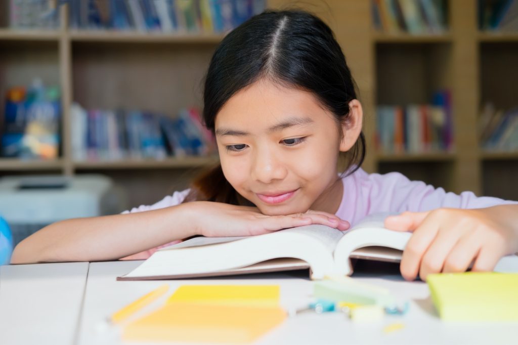 School girl reading book in library.