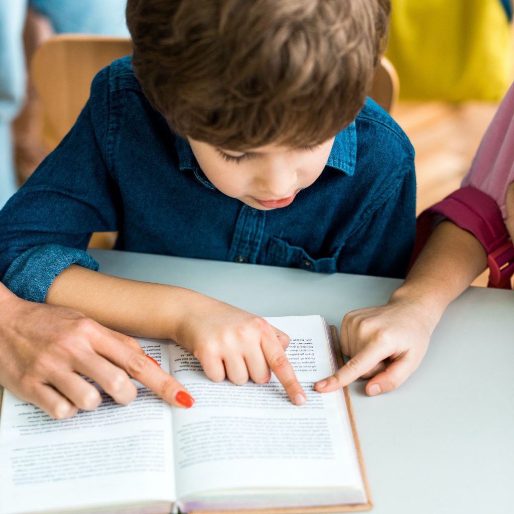 cropped view of woman and child pointing with fingers at book near boy